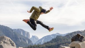Dynamic action shot of a man jumping over rocks with Yosemite's distinctive mountains in the background.